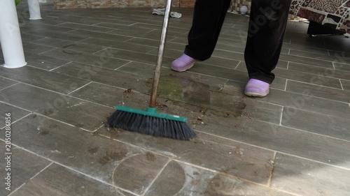 A woman removes trash from the floor of a house. A woman sweeps dust from a house.