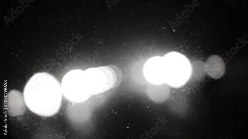 Blurred white car headlights traveling on a dark road in the night with dirt particles on the window