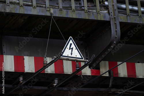 An overhead line warning sign for trams on a bridge. A triangular sign with a black lightning bolt on a white background to warn of high voltage electricity. These lines are used by trams. 