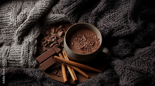 Dark and moody hot chocolate served on a wooden board with cinnamon sticks and chocolate chunks nestled in a grey knit blanket