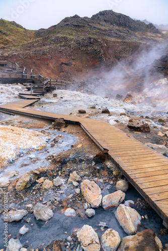 vertical photography of wooden walkways passing above the boiling water pool in Seltun, a geothermal area in Reykjanes Peninsula in Iceland on a spring day
