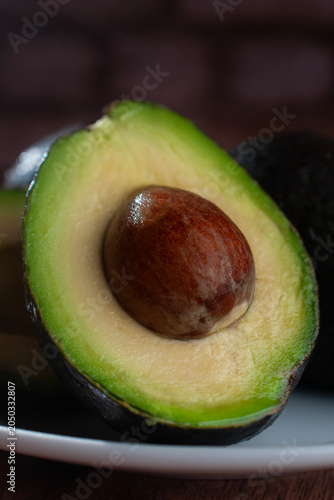 Freshly cut Hass avocado, halved, on a white plate against a dark background, with a close-up or macro vertical photograph