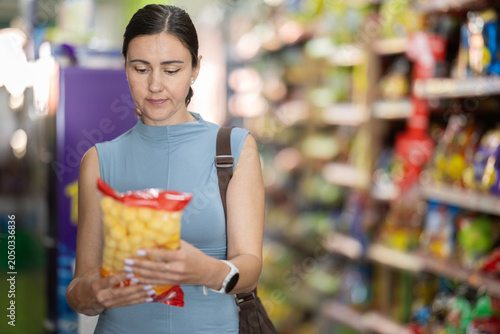 Foto In supermarket woman choose snacks, examines packages of food
