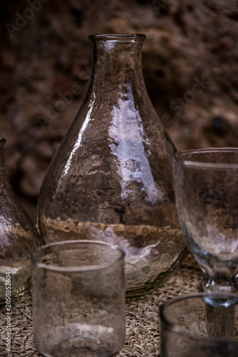 Old glass containers. Collection of retro bottle, amphorae and glasses placed on a wicker tray.
