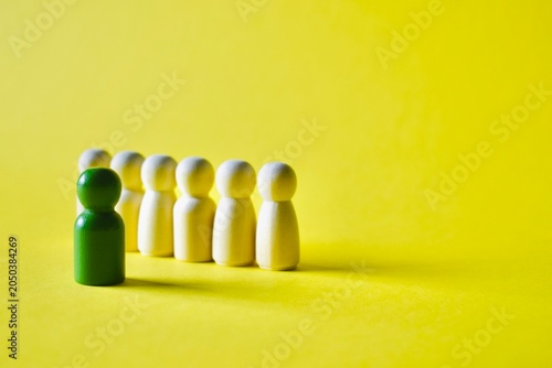 Tableau sur toile Angled perspective of a green wooden peg doll standing ahead of a diagonal line of white figures on a yellow background, conceptualizing leadership, guiding a team, or business pioneer