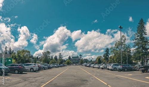 Wide parking lot, cars, and a building under a bright blue sky with puffy white clouds