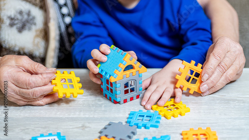 Grandparents And Child Building Toy House Together During Family Time At Home