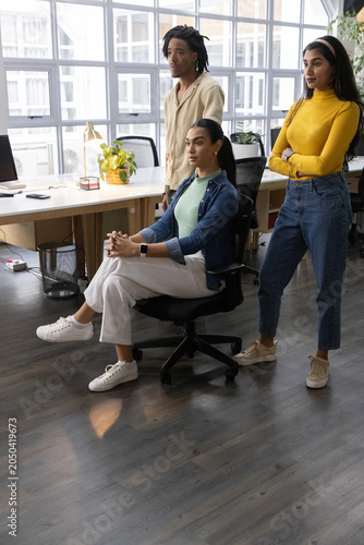 Diverse coworkers standing and sitting in modern office, reviewing computer monitor near desk