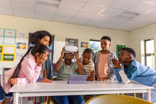Obraz na plátně Diverse preteen classmates gathering in class, watching peer using white VR head