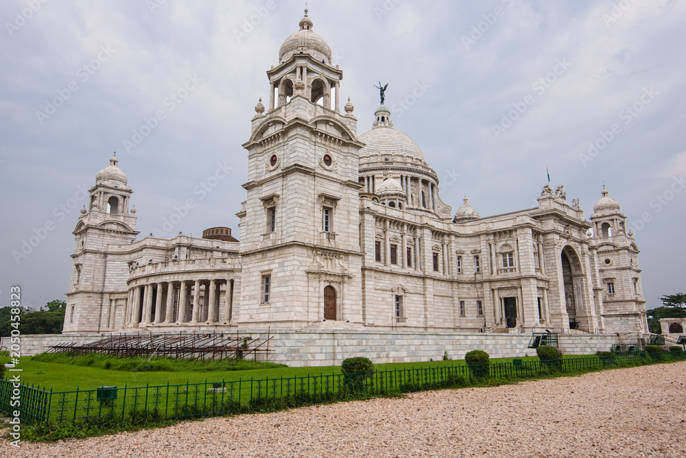 Obraz premium Front view of Victoria Memorial, the iconic white marble monument in Kolkata, India, surrounded by lush green gardens under a clear blue sky.
