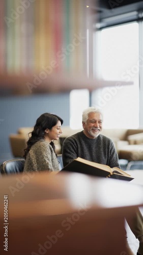 Elderly man enjoys time with young woman in a cozy library setting during a quiet afternoon