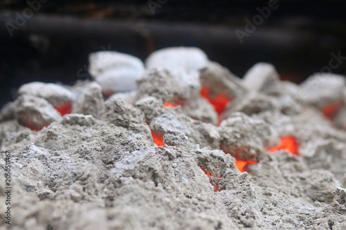 Obraz na plátně Closeup of glowing embers beneath a layer of cool gray ash, with soft orange light shining through the uneven charcoal texture in a hot, slowly fading firebed