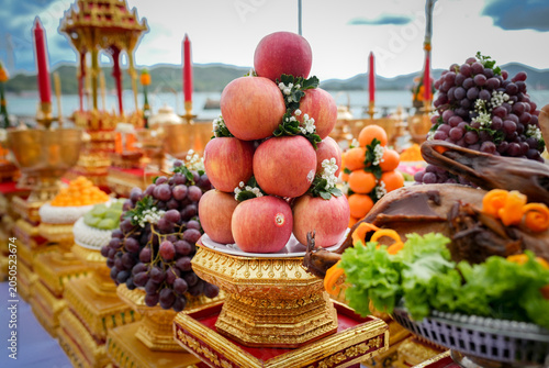 Fruit offering altar ceremony candle gold tray temple display beside river, stacked apple and grape arrangement on ornate pedestal, festive spiritual ritual atmosphere near mountain lake