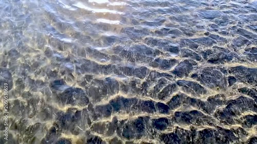Slow motion of water with sun-glints, flowing over a sandy bottom