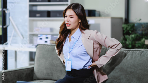 Schilderij op canvas Young businesswoman in office sitting on sofa and holding her lower back in pain