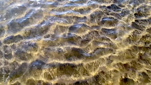 Slow motion of water flowing above the black and gold sandy bottom