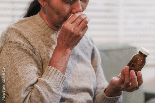 Konstfotografi Close-up of an unwell woman sitting indoors, covering her mouth while coughing and holding a medicine bottle, showing cold, flu, or respiratory illness at home