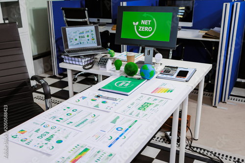 Office desk with net zero and esg reports, charts, laptop and monitor, workplace focused on sustainability, carbon reduction and green business planning.