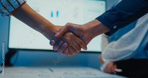 Close up multiracial group young Asia businesspeople in smart casual wear discussing business shaking hand together while stand in modern night office. Partner cooperation, coworker teamwork concept.
