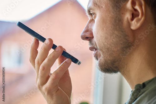 Принти на полотні Closeup side view of man speaking into smartphone near window in daylight