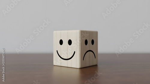 A wooden cube with two faces, one smiling and one frowning, on a brown surface