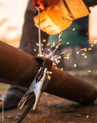 Grounding clamp connected to steel pipe highlights essential role of electrical conductivity in welding operations. Industrial detail focused on safety, efficiency and stable fabrication results.