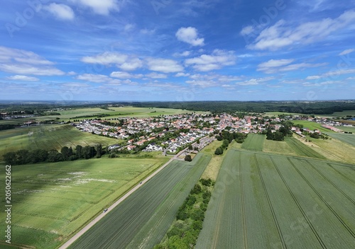 Village d'Haucourt Moulaine, en Meurthe et Moselle, Lorraine. Vue aérienne panoramique de la commune, ses habitations et ses bâtiments au milieu des champs et des cultures. Ciel bleu nuageux.