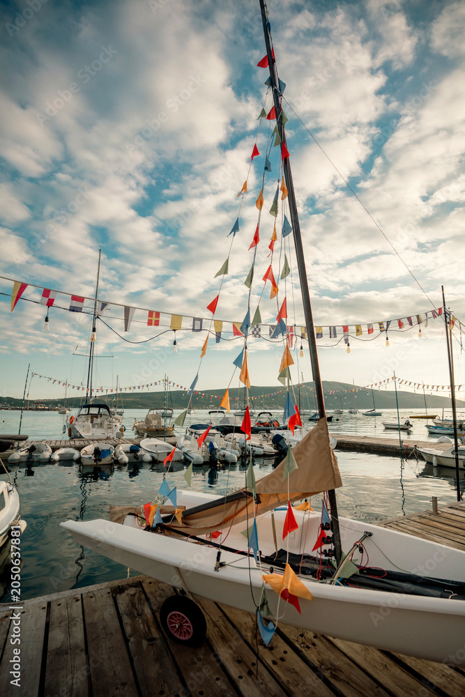 Obraz premium Little sailboat docked at a wooden jetty with vibrant pennant flags, children sailing camp adventure concept.