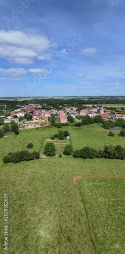 Vue aérienne panoramique du village de Laix, en Meurthe-et-Moselle, Lorraine. La commune rurale avec ses habitations et ses bâtiments entourée de champs et de cultures. Ciel bleu et nuages
