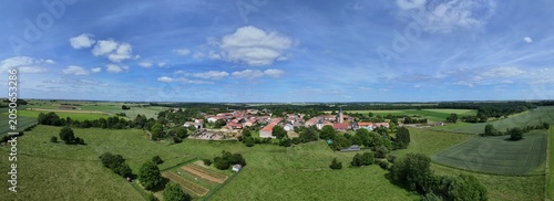 Vue aérienne panoramique du village de Laix, en Meurthe-et-Moselle, Lorraine. La commune rurale avec ses habitations et ses bâtiments entourée de champs et de cultures. Ciel bleu et nuages
