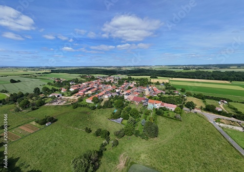 Vue aérienne panoramique du village de Laix, en Meurthe-et-Moselle, Lorraine. La commune rurale avec ses habitations et ses bâtiments entourée de champs et de cultures. Ciel bleu et nuages