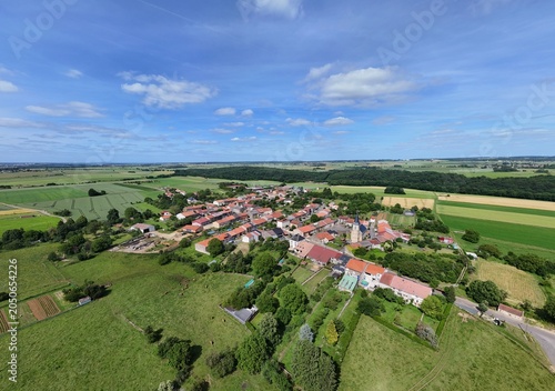 Vue aérienne panoramique du village de Laix, en Meurthe-et-Moselle, Lorraine. La commune rurale avec ses habitations et ses bâtiments entourée de champs et de cultures. Ciel bleu et nuages