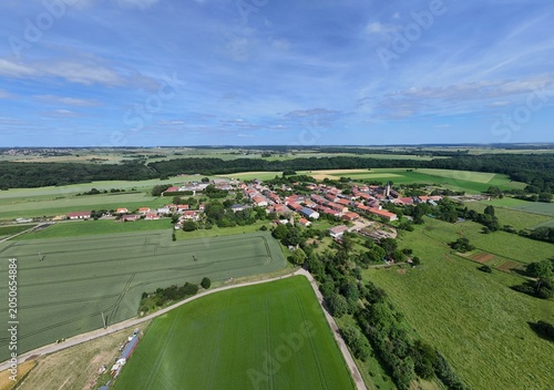 Vue aérienne panoramique du village de Laix, en Meurthe-et-Moselle, Lorraine. La commune rurale avec ses habitations et ses bâtiments entourée de champs et de cultures. Ciel bleu et nuages