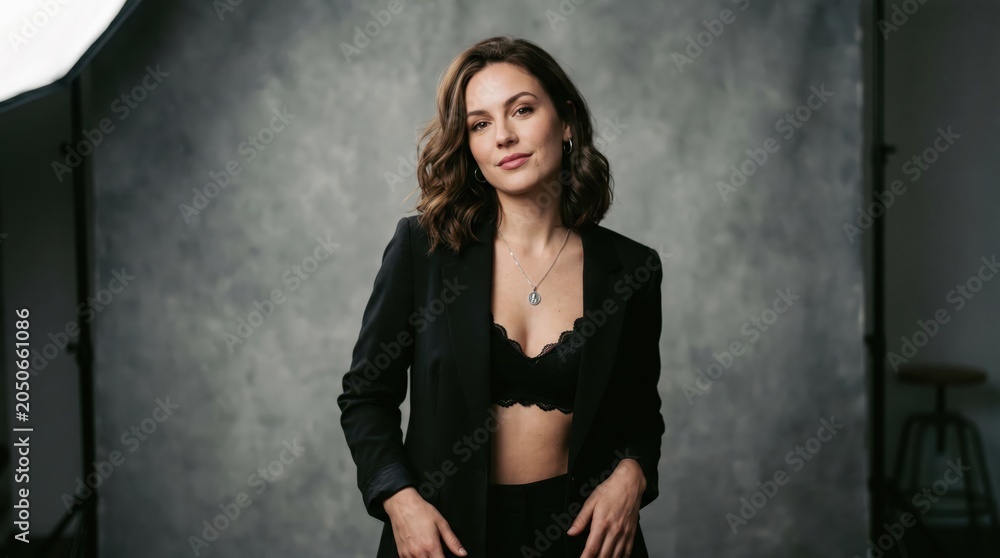 Fototapeta premium Studio portrait of a young brunette in a black lace bra and jacket against a gray backdrop.