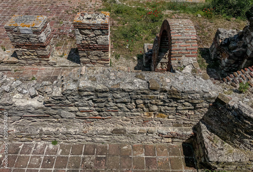 Landscape high angle full frame view of historical archaeological site featuring ancient stone walls, brick pillars, and a ruined masonry archway