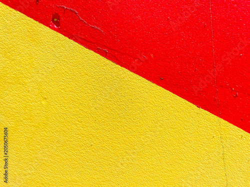 Landscape close up full frame view of a rough granular textured wall painted diagonally in vibrant bright red and solid yellow blocks