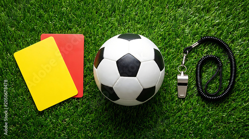 Soccer referee equipment including a ball, whistle, and yellow and red cards on green grass