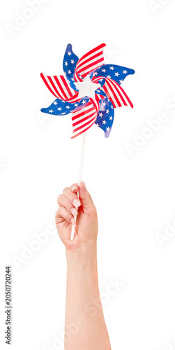 Female hand holding a colorful plastic pinwheel windmill decorated with the American flag pattern red, white, and blue with stars. Isolated on a white background. Perfect design element for 4th July