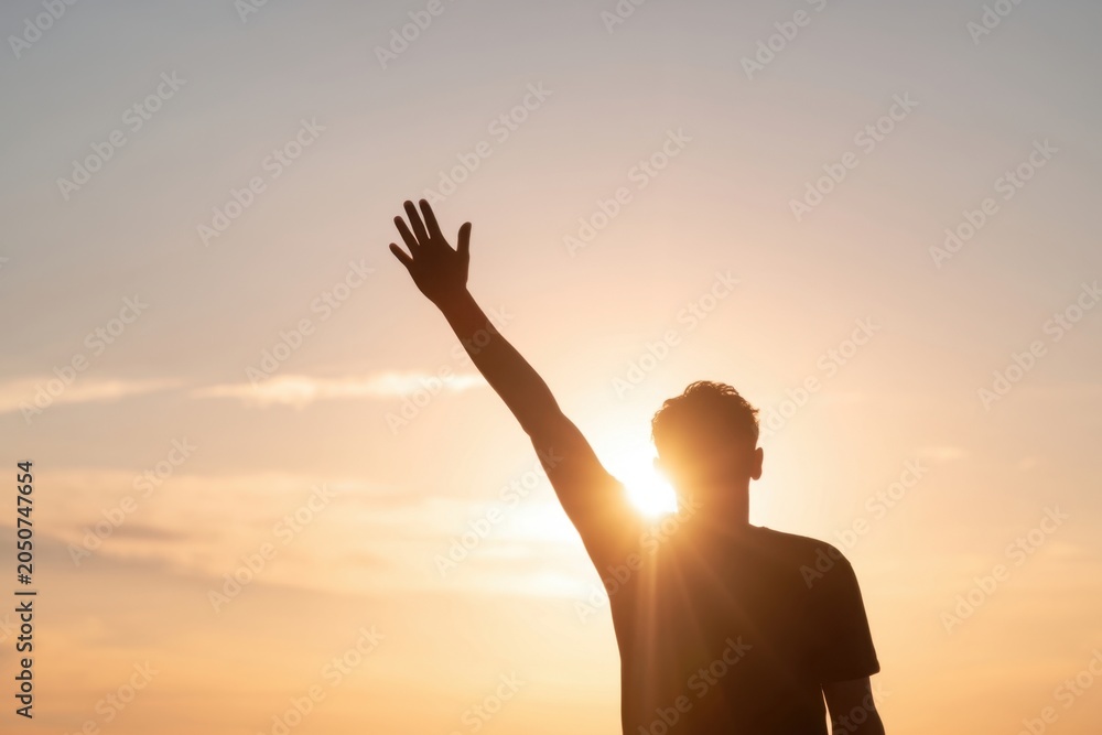 Fototapeta premium The person silhouetted against a golden sunset raising a hand toward the sky