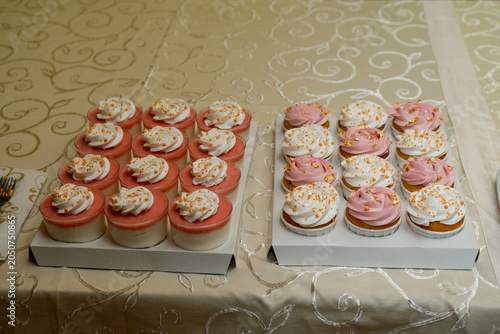 pink and white muffins next to which small boxed cheesecakes are lined up and ready to serve