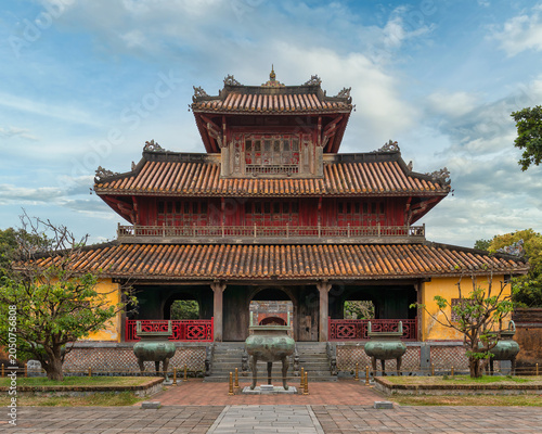 Hien Lam Cac pavilion, Imperial City, Hue, Vietnam. Traditional Vietnamese architecture with red and yellow tiers, ornate roofs, and bronze urns under a cloudy sky