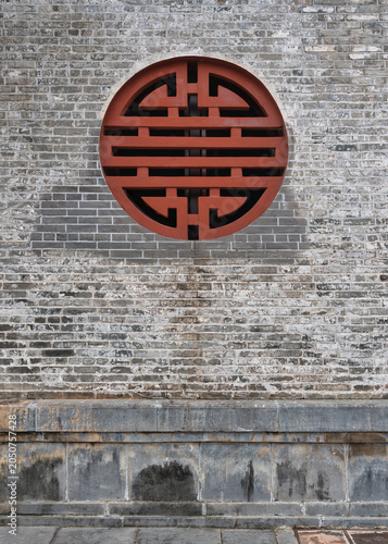 Traditional red circular window with a stylized Shou symbol on an aged grey brick wall, showcasing ancient Vietnamese architecture in Hue, Vietnam