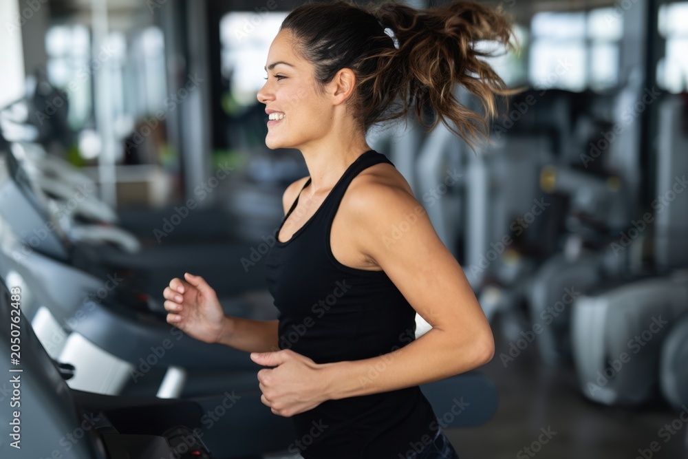 Fototapeta premium The woman running on a treadmill in a modern gym smiling during workout