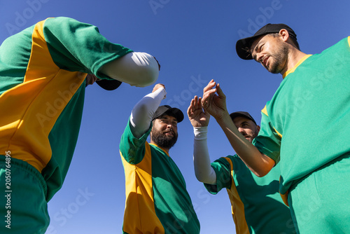 Vertical video: Raising hands four athletes starting pre-game huddle at field in green jerseys
