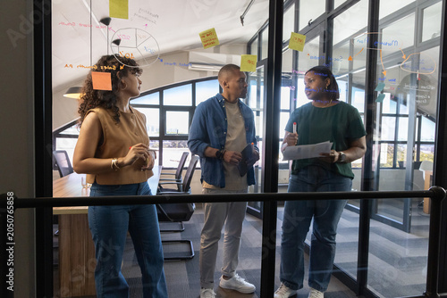 Foto Diverse team annotating glass wall with sticky notes and papers in office in cas
