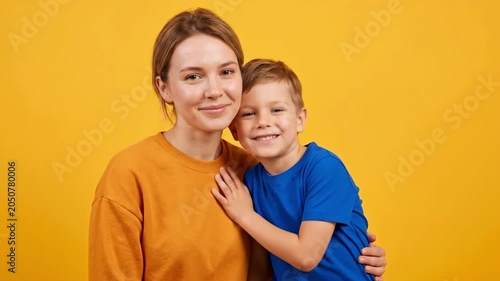 Smiling woman hugging young boy on yellow background. Happy mother and son portrait for family togetherness and international Missing Children Day awareness