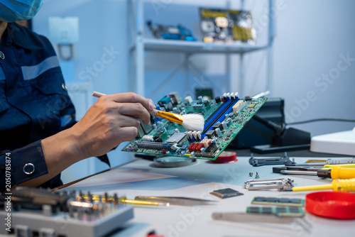 Bild auf Leinwand Technician cleaning and repairing a computer motherboard at an electronics workbench with tools, showing careful maintenance, hardware service, and modern technology support