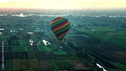 A lone hot air balloon floats silently over the exceptionally lush agricultural floodplains of the Nile River's West Bank at sunrise.