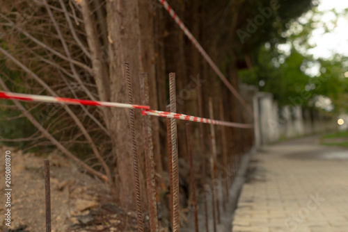 Fotografi Rusty steel rebar stakes driven into the ground form a makeshift barrier beside a paved sidewalk