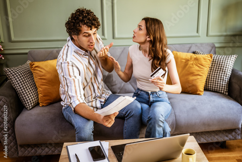 Couple discussing their expenses while examining home finances. They are checking financial documents and calculating family budget in their living room.